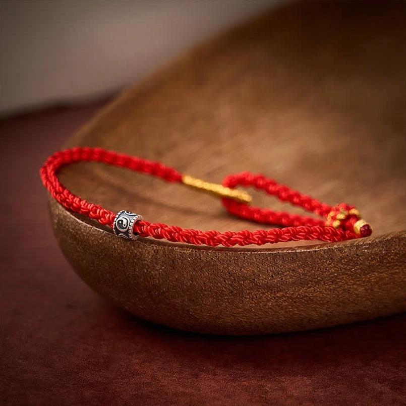 Adjustable red string Yin Yang bracelet with silver bead on wooden surface