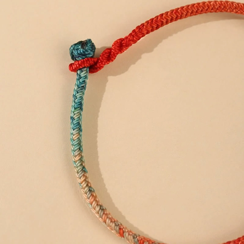 Red string bracelet close-up showing teal gradient weave and natural material craftsmanship