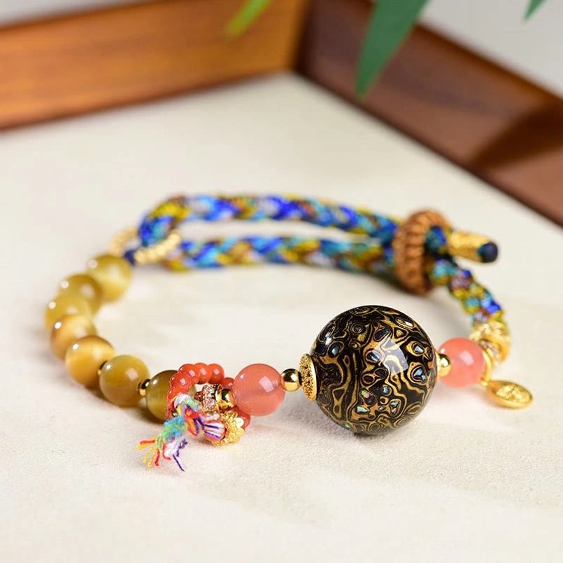 Hand woven red string protection bracelet with Tibetan lacquer bead and tassel on wooden trim desk
