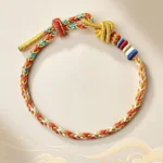 Handcrafted colorful Tibetan red string braided bracelet with gold accents on beige cloud background