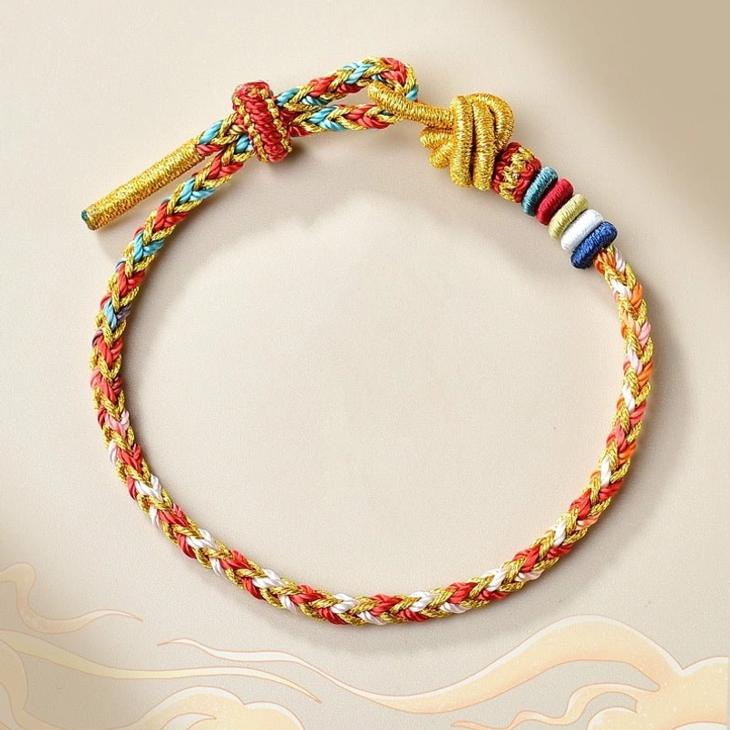 Handcrafted colorful Tibetan red string braided bracelet with gold accents on beige cloud background