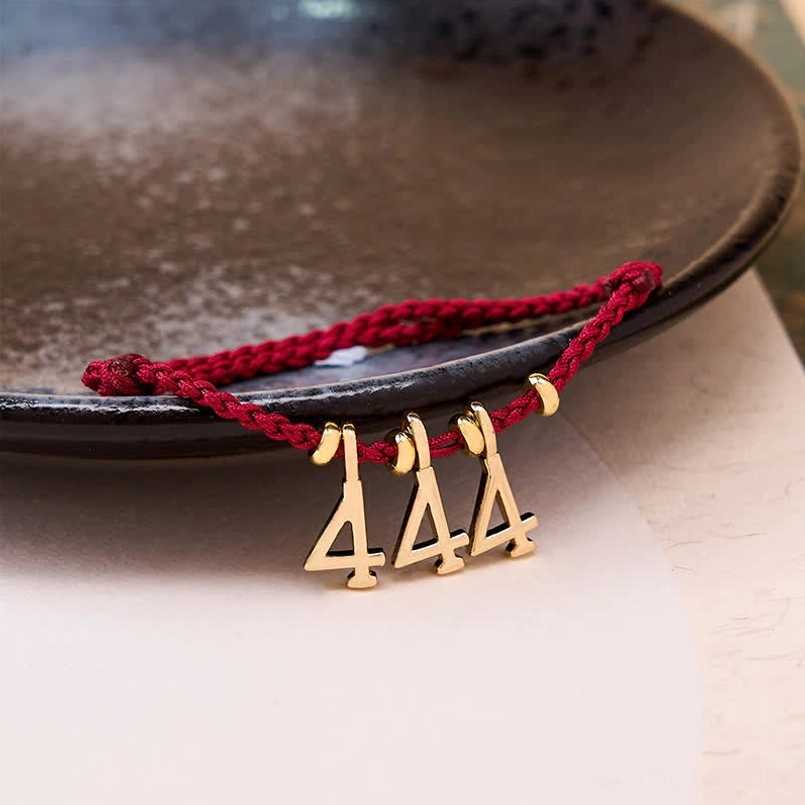 Handmade red braided cord bracelet with gold angel number charms - flat lay styling