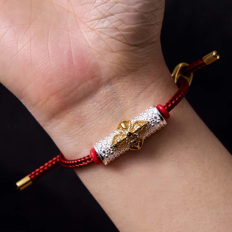 Red string bracelet with precious metal accents and handcrafted flower charm design