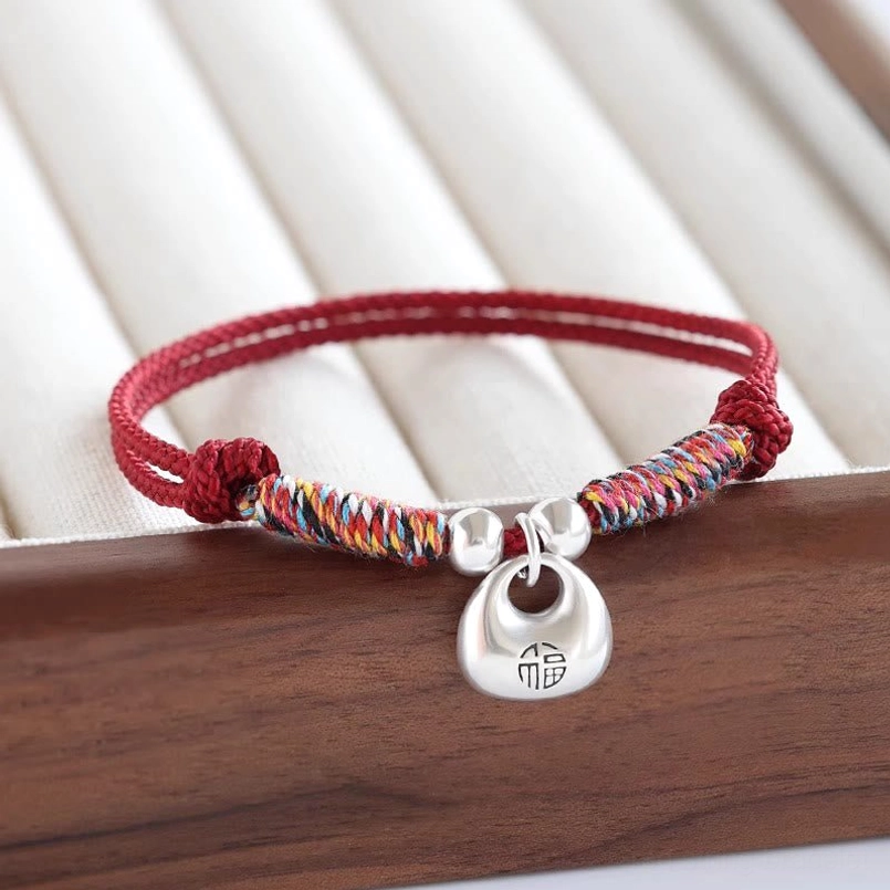 Red braided lucky bracelet with 925 sterling silver Fu lock pendant on wooden tray