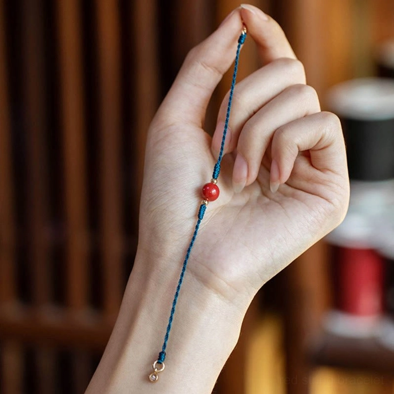 Handheld close up of unfastened adjustable blue cord cinnabar bracelet in workshop
