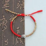 Handmade Buddha head woven red string bracelet flat lay on Chinese calligraphy background