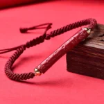 Handmade cinnabar braided red string bracelet with engraved Om Mani Padme Hum charm on wooden display block