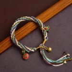 Handmade multicolor red string bracelet with golden Swallowing Beast charms on dark wood background