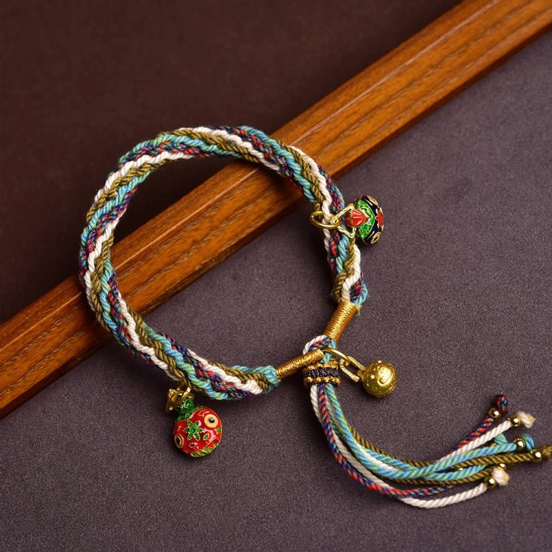 Handmade multicolor red string bracelet with golden Swallowing Beast charms on dark wood background