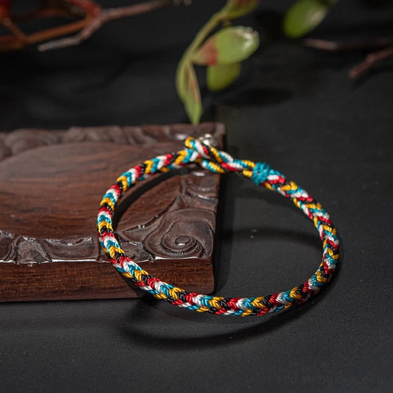 Tibetan five color woven red string bracelet side oblique view with green foliage