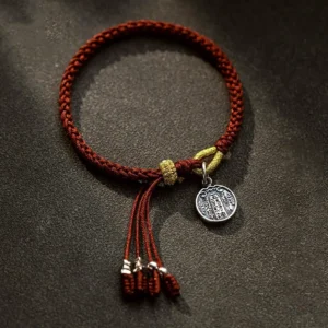 Five Directions Gods of Wealth red string bracelet flat lay on dark brown tabletop