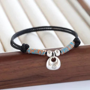Black braided red string bracelet with 925 sterling silver Fu charm on wooden tray