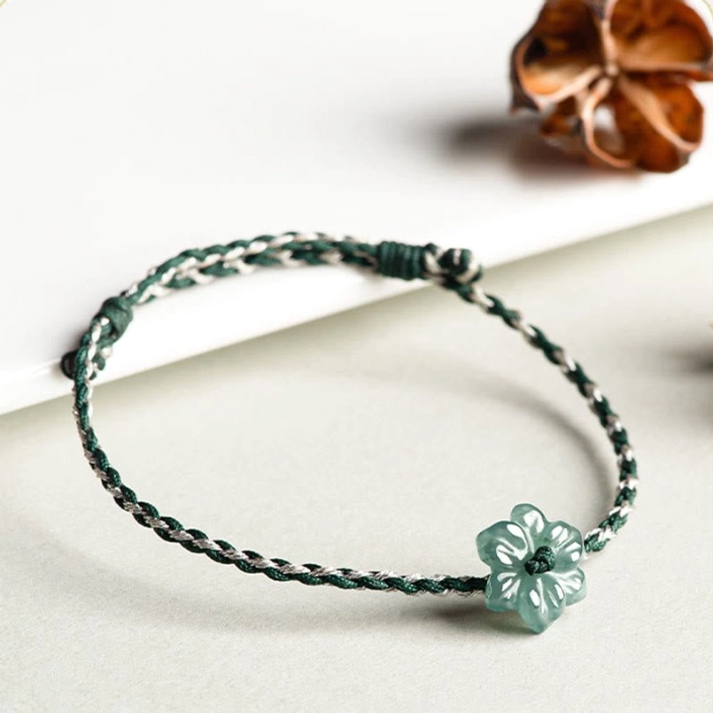 Flat lay view of dark green braided jade orchid bracelet on light desk with dried decor