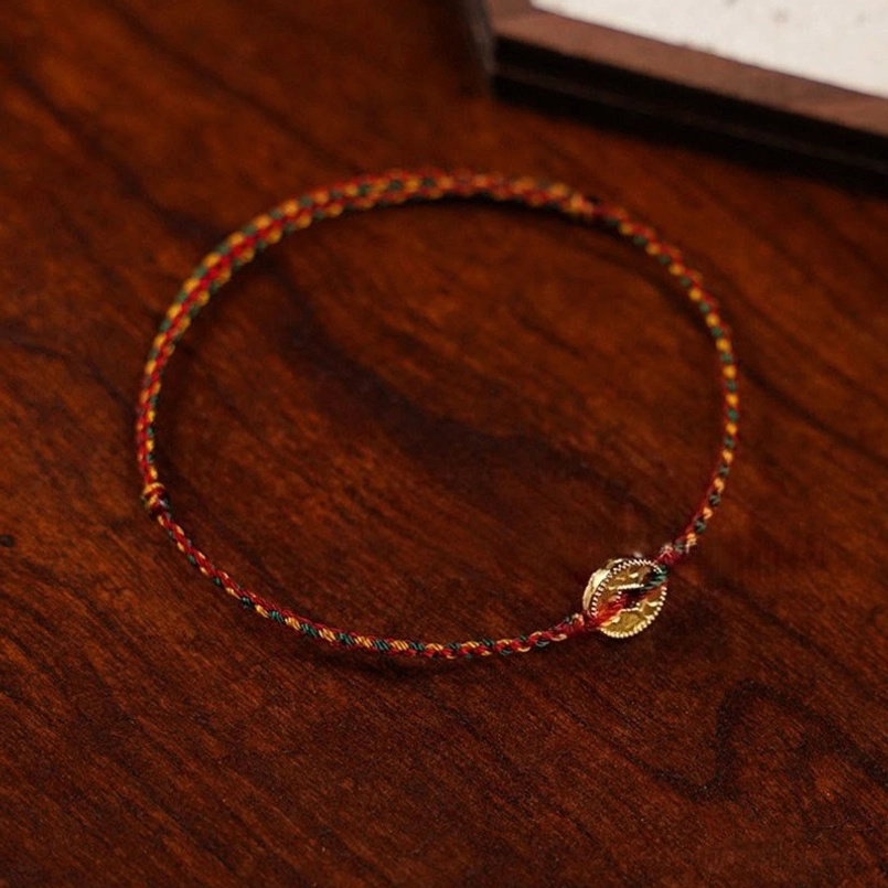 Tibetan Buddhist red string copper coin charm bracelet flat lay on wooden surface