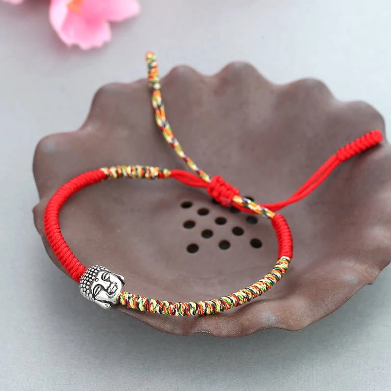 Handmade serenity Buddha red string bracelet on brown ceramic dish with pink flower