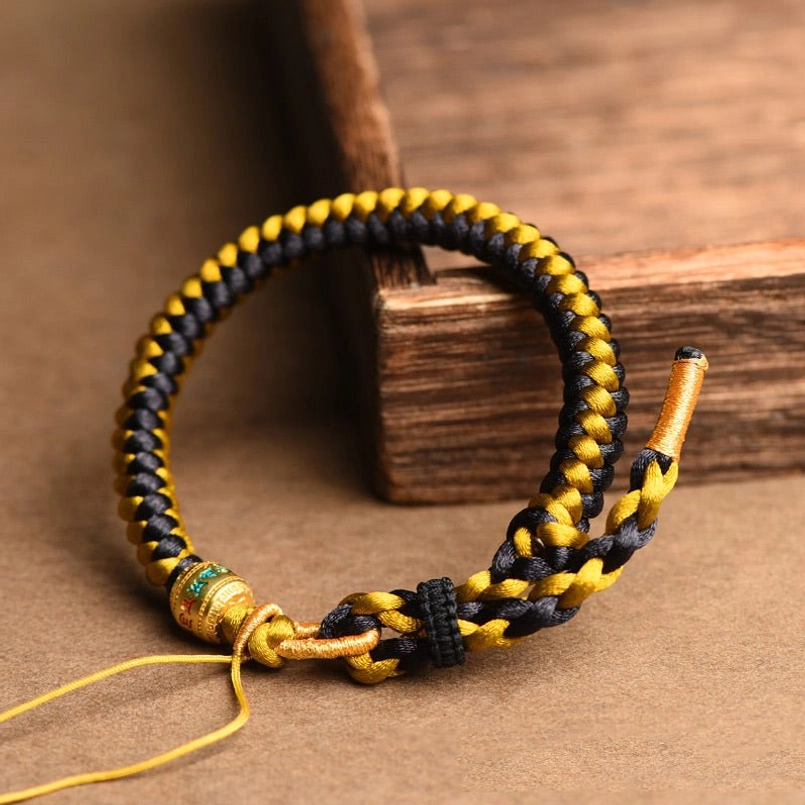 Tibetan luck bracelet side view with enamel metal bead and adjustable tail strings on wooden prop