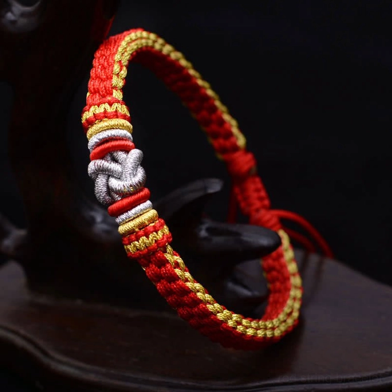 Handmade woven friendship bracelet with red gold and silver knot decor on dark wooden stand