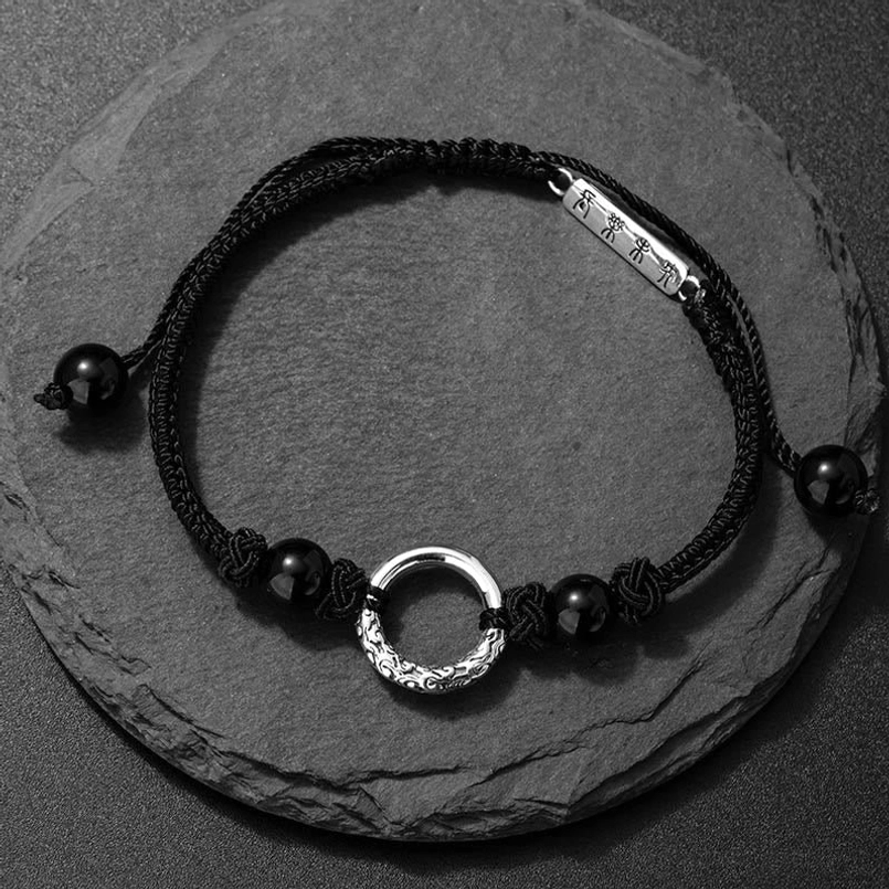 Front top-down view of black onyx peace buckle string bracelet on dark slate