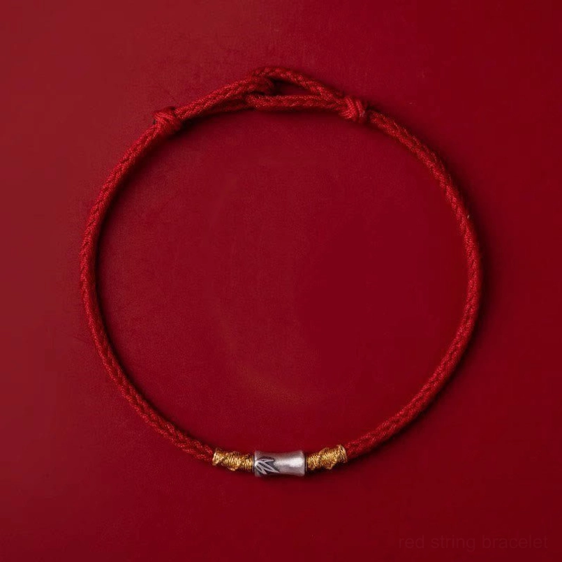 Braided red luck bracelet with twisted metal detail on dark red background