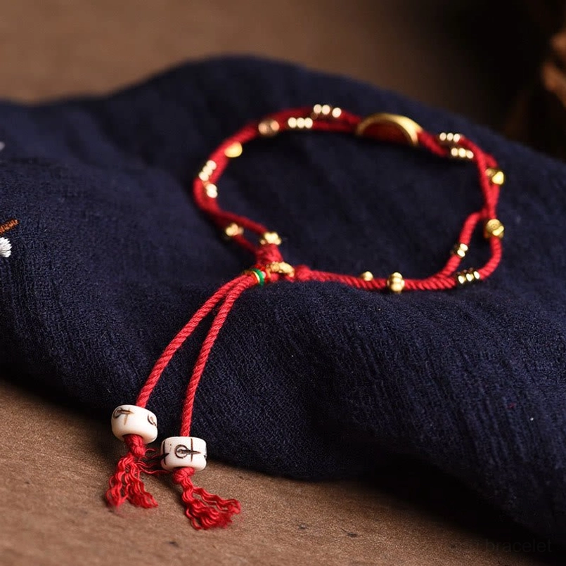 Double layer red rope bracelet with cinnabar charm on brown wooden table