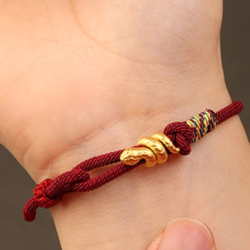 close up woven texture of gold snake red string bracelet on human skin
