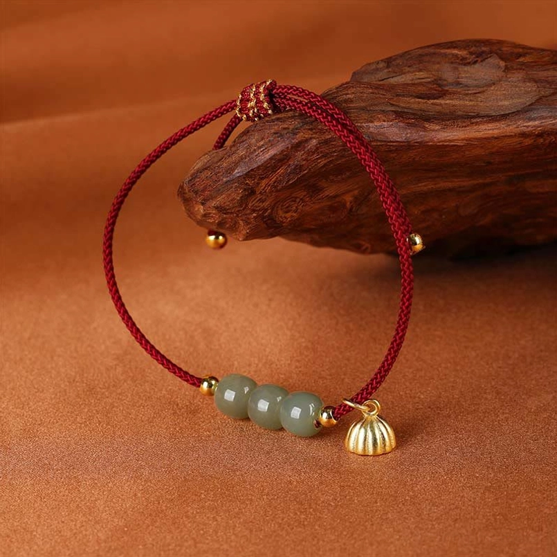 Red string Hetian jade bracelet with lotus pod charm next to wooden home decor