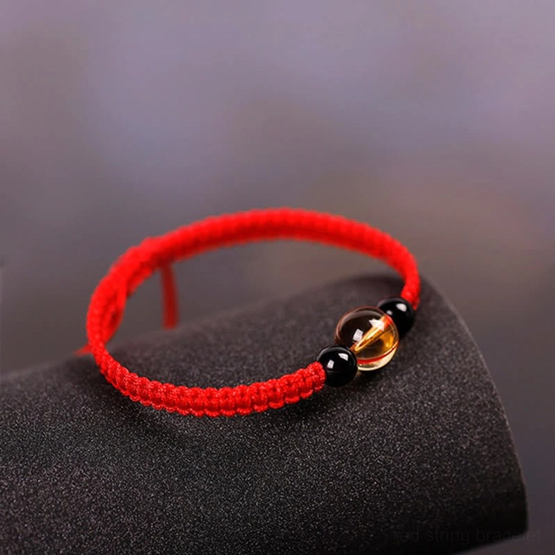 Red string beaded bracelet flat lay on matte black display mount