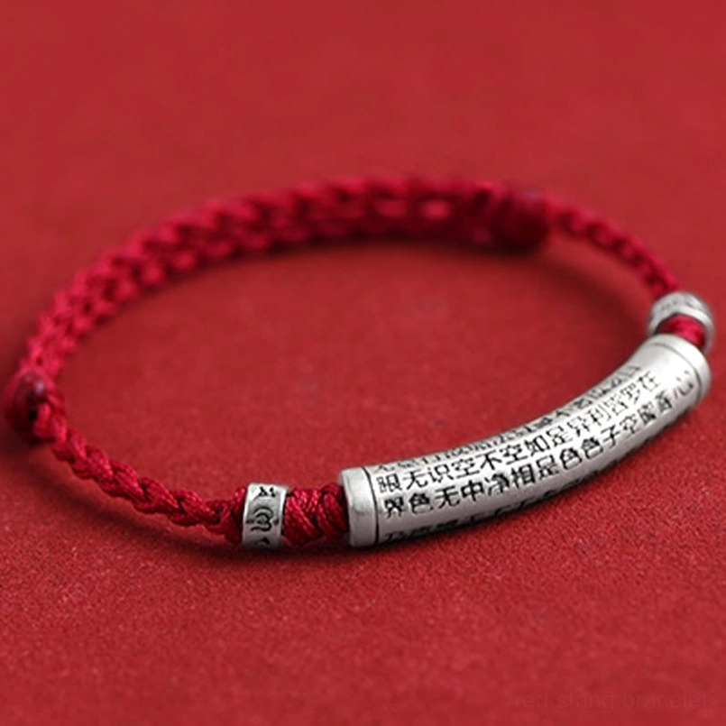Close-up top view of Heart Sutra bracelet displaying intricate 3D carved silver charm on red background