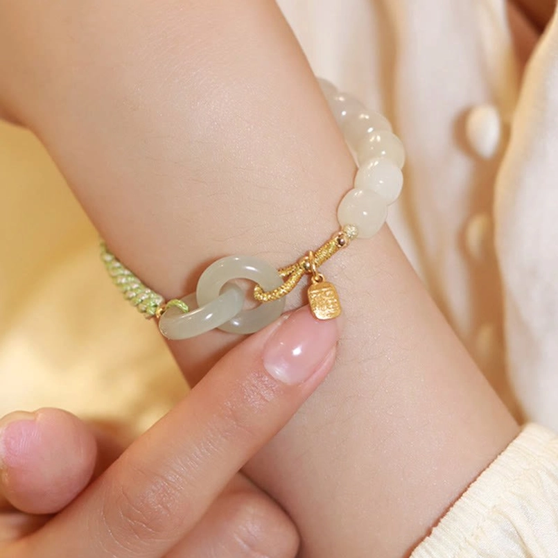 Close-up of Hetian jade beaded bracelet with round milky white beads green woven rope and gold fu character charm