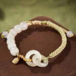 Hetian jade double peace buckle fu character abundance bracelet with green braided cord and gold accents on brown velvet