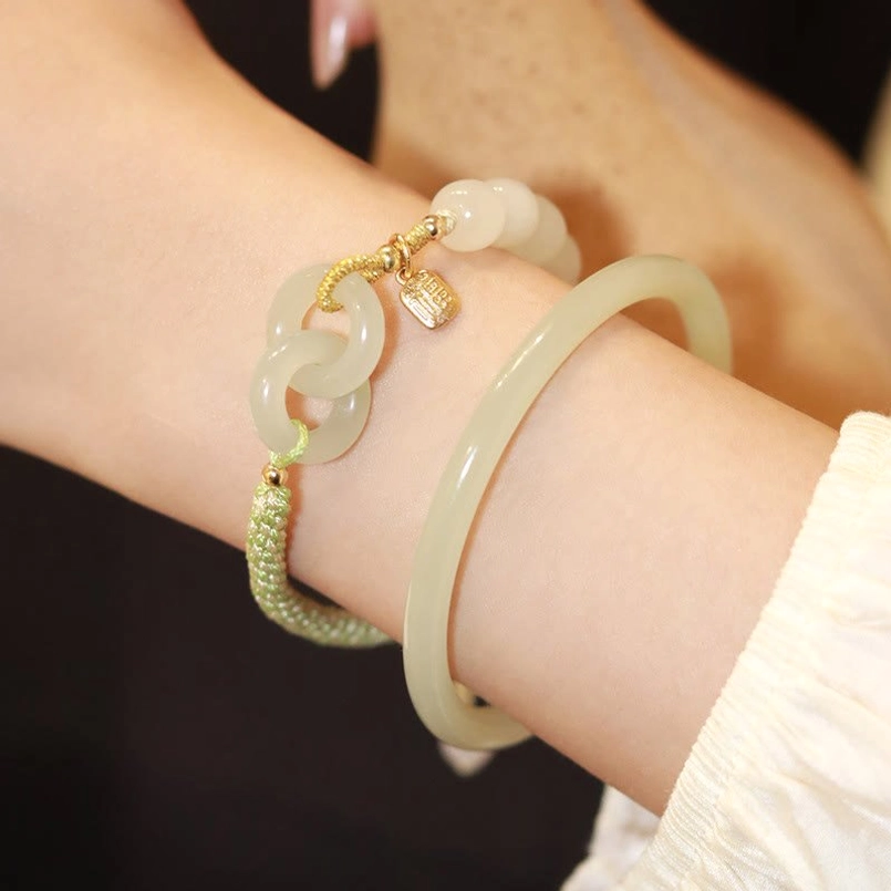 Woman's wrist wearing Hetian jade double peace buckle bracelet with natural stone variations and gold accents