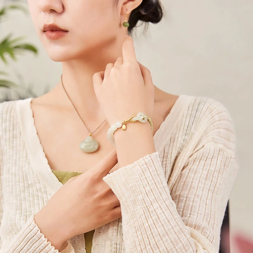 Woman in beige sweater wearing Hetian jade double peace buckle bracelet with matching jade necklace casual style