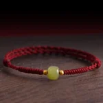 Hetian jade and gold red string bracelet overhead side view on dark wood