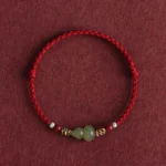 Dark red rope Hetian jade gourd protection bracelet flat lay with green jade charm and silver accent beads