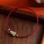 Hetian jade gourd red string bracelet with silver beads on dark wooden background, top-down view
