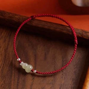 Hetian jade gourd red string bracelet with silver beads on dark wooden background, top-down view