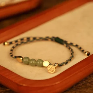 Hetian jade lotus braided bracelet flat lay with two-tone woven cord and green jade beads on wooden display tray