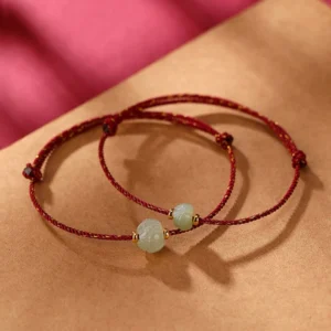 Twin Hetian jade lotus red string bracelets with gold-plated sterling silver accents on textile background