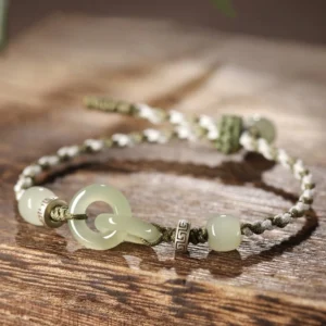Hetian jade peace buckle braided bracelet with interlocking jade buckles and two-tone braided cord on wooden surface