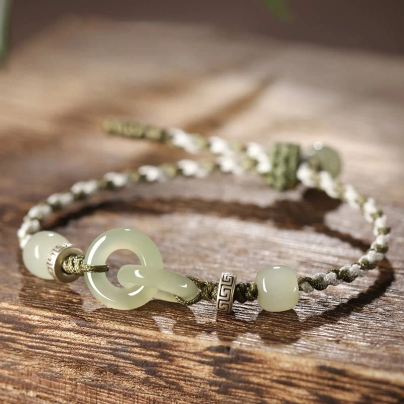 Hetian jade peace buckle braided bracelet with interlocking jade buckles and two-tone braided cord on wooden surface
