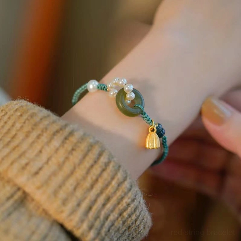 Hetian jade peace buckle bracelet with pearl and gold lotus charm worn on wrist with knitted sweater