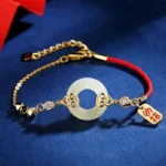 Hetian jade peace buckle red string bracelet with sterling silver and zircon, three-quarter view on dark blue background