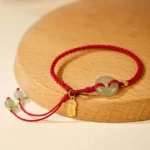 Natural Hetian jade peace buckle red string bracelet with gold accents on wooden display