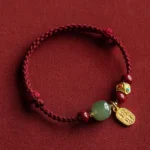 Hetian jade prosperity bracelet with five-colored red string and gold charm, flat lay display on dark fabric