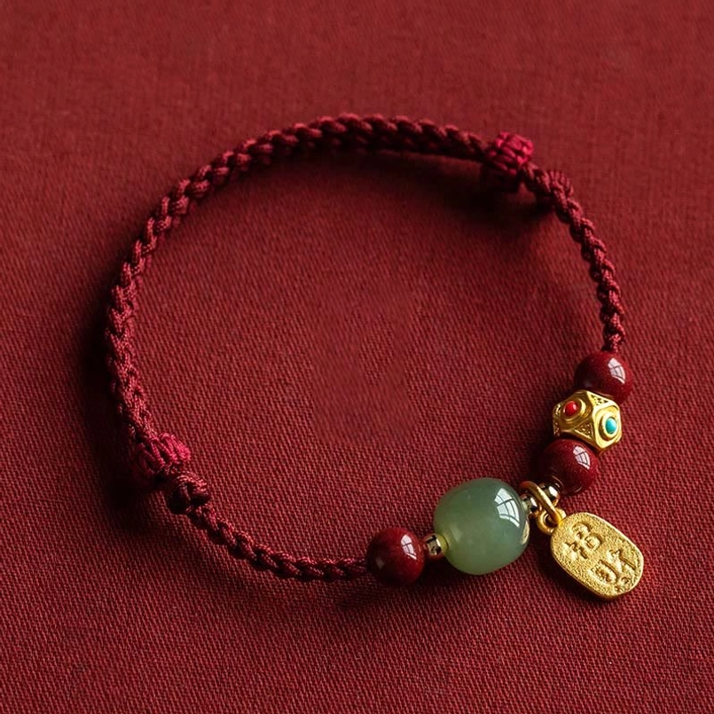 Hetian jade prosperity bracelet with five-colored red string and gold charm, flat lay display on dark fabric