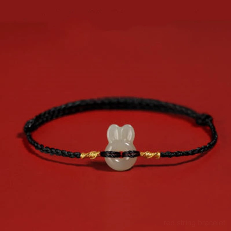 Black string Hetian jade rabbit bracelet with gold accents on dark red background