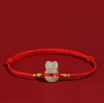 Red string Hetian jade rabbit bracelet with gold knots on dark background