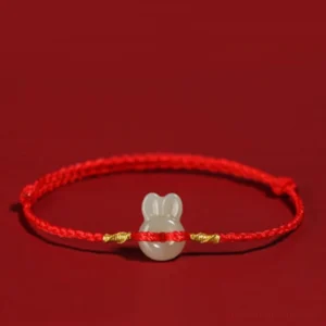 Red string Hetian jade rabbit bracelet with gold knots on dark background