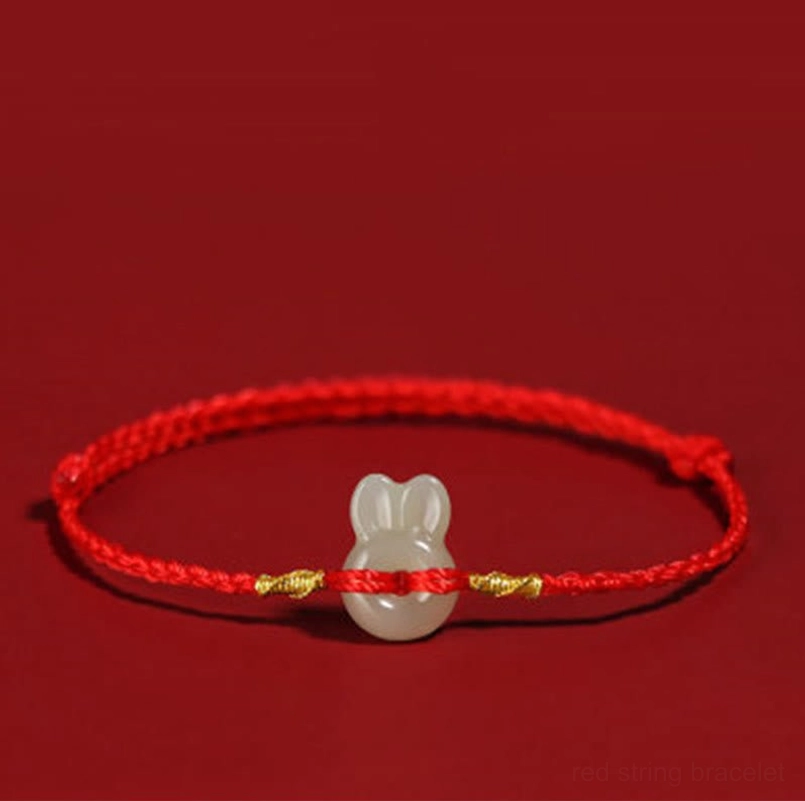 Red string Hetian jade rabbit bracelet with gold knots on dark background