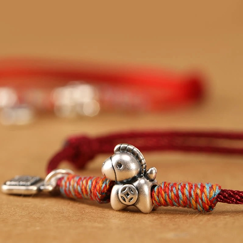 Side profile view of Year of the Horse zodiac luck bracelet with silver charms and braided red cord